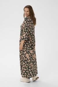 Maxi dress in dark green fabric with peach leopard print, featuring three-quarter sleeves and a cinched waist. Worn with light-colored sneakers.