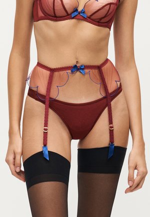 Vrouw draagt een bordeauxrode lingerieset met een transparante jarretelriem versierd met blauwe strikjes en bevestigd aan zwarte kousen tot mid-dij.