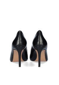 Tacones altos de cuero negro con punta afilada, textura suave, tacón de aguja y plantilla marrón, con un diseño minimalista y costuras sutiles.