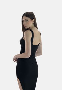 Abito nero aderente con spalline sottili, schiena scoperta e una fessura alta fino alla coscia sul lato sinistro, realizzato in un tessuto morbido e elasticizzato.