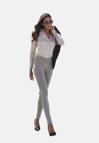 Helle beige Button-up-Bluse, graue karierte, taillierte Hose, schwarzer Blazer über dem Arm, dunkle Sonnenbrille und schwarze High Heels.