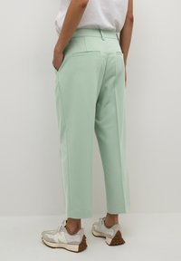 Pantalon ajusté vert menthe avec jambe droite, poches latérales et arrière, associé à des baskets crème avec semelles texturées.