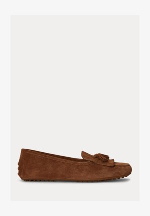 Mocassin plat en daim marron avec pompon et semelle en caoutchouc cloutée, vue de côté sur fond clair uni.