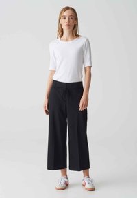Zwarte wijde broek met een drawstring taille, gecombineerd met een strakke witte T-shirt met korte mouwen en witte sneakers met rode accenten.