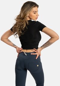 Haut ajusté noir à manches courtes associé à un legging taille haute bleu marine avec deux poches arrière et des détails de couture décoratifs.