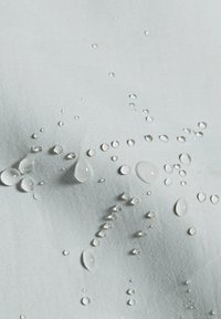 Σταγόνες νερού που σχηματίζονται σε μια επιφάνεια υφάσματος ανοιχτό γκρι, που δείχνουν υφή αδιάβροχου ή ανθεκτικού στο νερό υλικού.