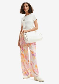 T-shirt blanche à rayures, pantalon large en imprimé aquarelle pastel dans les tons rose et orange, et sac surdimensionné blanc avec logo en relief. Baskets.