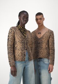 Twee cardigans met een luipaardprint, waarvan de ene een bruin-zwarte knoopsluiting heeft en de andere een diepe V-hals. Beide hebben een gestructureerde stof.