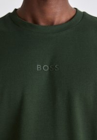 T-shirt en coton vert avec un col rond classique. Équipé d'un logo en caoutchouc noir en relief "BOSS" à l'avant. Texture douce et lisse.