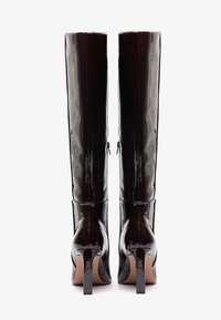 Bottes noires en cuir verni montantes avec une finition lisse et brillante, des talons carrés et un design ajusté. Dotées de zips à l'arrière.