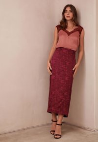 Rózsaszínű szatén felső csipkerészletekkel, hosszú bordó szoknyával, mely élénk virágmintás textúrával díszített. Fekete bokapántos magassarkú.