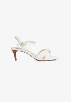Sandalo bianco in pelle con tacco kitten, cinturini intrecciati sulla punta, cinturino alla caviglia con fibbia dorata e tacco con effetto legno su sfondo bianco.