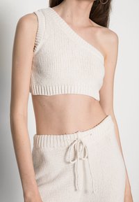 Top cropped de malha branca com uma alça, apresentando uma textura canelada e uma silhueta ajustada, combinado com calças de malha de cintura alta na mesma cor.