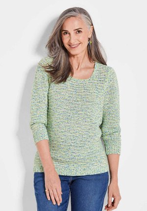 Strickpullover in Pastellgrün mit blauen und gelben Sprenkeln. Verfügt über einen runden Ausschnitt und 3/4-lange Ärmel. Kombiniert mit blauen Jeans.