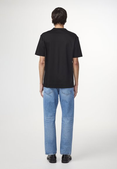 T-shirt noir à manches courtes avec un col rond, associé à un jean droit bleu clair et des chaussures noires. Design simple et épuré.