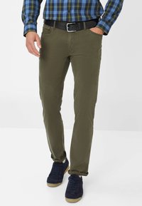 Pantalon en coton vert avec une coupe slim, doté de poches avant et d'une ceinture. Assorti avec des chaussures en daim bleu foncé et une chemise à carreaux.