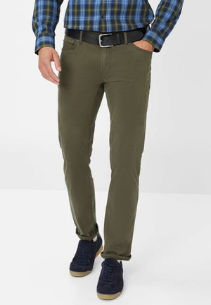 Groene katoenen broeken met een slim fit, voorzien van voorzakken en een riem. Gekleed met donkerblauwe suède schoenen en een geruit shirt.