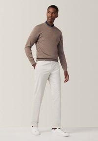 Hellbrauner Pullover mit Rundhalsausschnitt, beigen maßgeschneiderten Hosen und weißen Sneakers. Das Outfit zeichnet sich durch ein minimalistisches Design und klare Linien aus.