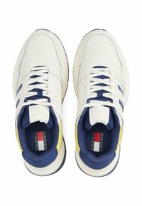 Białe sneakersy z teksturowaną cholewką, granatowymi akcentami i żółtym detalem na pięcie. Posiadają sznurowanie oraz wielokolorowe logo wewnątrz.