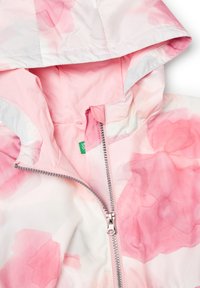 Giacca a fiori rosa con cappuccio, realizzata in tessuto leggero. Presenta una zip argentata e un'etichetta interna verde.