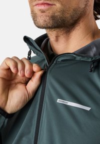 Giacca softshell verde con zip davanti, dotata di un patch con logo, cappuccio regolabile e materiale leggero e resistente all'acqua.