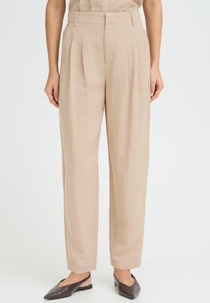 Pantalones beige plisados con cintura alta, silueta de pierna recta y textura suave. Combinados con bailarinas oscuras de punta puntiaguda.