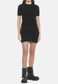 Top nero a maniche corte, aderente; gonna a portafoglio nera con design drappeggiato e dettagli ritagliati; stivaletti neri massicci con cinturini sovrapposti.