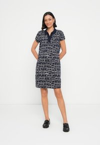 Μπλε σκούρο φόρεμα με κοντά μανίκια και γιακά, με γεωμετρικό λευκό σχέδιο. Κατασκευασμένο από ελαφρύ ύφασμα, έχει ίσια γραμμή και μήκος μέχρι το γόνατο.