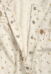 Tissu crème clair avec de petits motifs floraux en jaune et marron. Comprend des boutons pression en argent et un bouton décoratif en bois en forme de cœur.