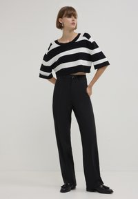 Gestreifter schwarz-weißer, verkürzter Pullover, kombiniert mit hochtaillierten schwarzen Hosen, die über einen Einzelknopfverschluss und ein elegantes Design verfügen.