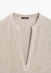 Beige gestructureerde linnen overhemdenkraag met een diepe V-hals en een zwart label met de tekst "Massimo Dutti Made in China".