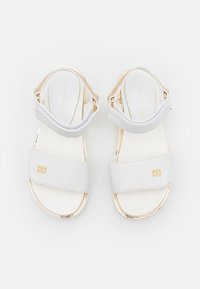 Białe sandały z złotymi akcentami, na płaskiej podeszwie, z dwiema szerokimi paskami. Posiadają małe logo na przednim pasku oraz teksturowany tylny pasek.