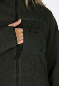 Groene fleecejack met een rits aan de voorkant, met een getextureerd bovenstuk en een borstzak die een geborduurd logo toont.
