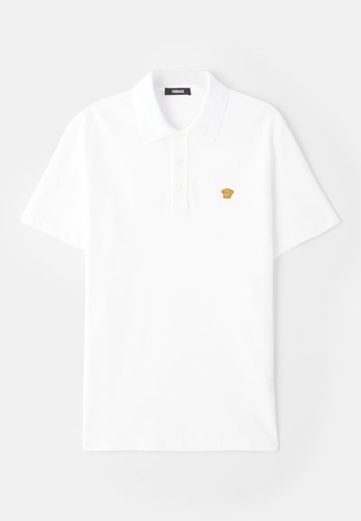 Baltas kokvilnas polo krekls ar klasisku apkakli, trīs pogu aizdari un mazu zelta logotipa detaļu kreisajā krūšu pusē.