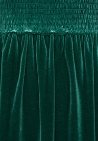 Robe en velours vert présentant un haut smocké avec une texture horizontale et des plis fluides en bas, mettant en valeur une couleur riche et profonde.