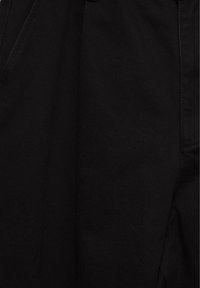 Gros plan d'un tissu en denim noir montrant la texture et les détails de couture d'un vêtement.