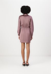 Robe en satin mauve avec des manches longues, une taille élastique et un col. Présente une texture lisse et arrive à mi-cuisse.