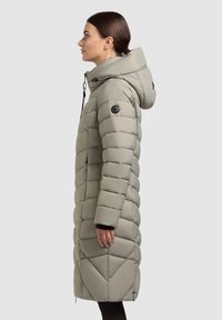 Vaaleanharmaa toppatakki hupulla, pidennetty malli, pystysuora tikattu kuvio, mustat yksityiskohdat hihojen resoreissa ja etiketeissä, vetoketjukiinnitys edessä.