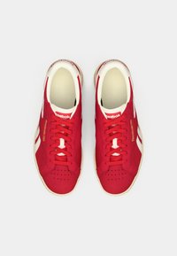 Scarpe da ginnastica rosse con accenti bianchi, caratterizzate da una tomaia in tessuto morbido, punta rotonda, design con lacci e dettagli perforati sulla parte anteriore.