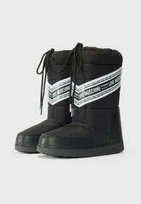 Fekete párnázott csizma texturált gumitalppal, fehér szalaggal, amelyen a "LOVE MOSCHINO" felirat szerepel, és állítható fekete fűzőkkel.