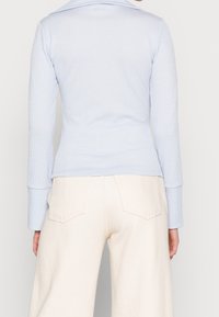 Haut à manches longues côtelé bleu clair avec un col, associé à un pantalon large crème avec deux poches arrière et une finition texturée.