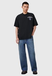 Sort bomulds T-shirt med korte ærmer og rund hals, med et grafisk design i pink og hvid på forsiden. Kombineret med blå denim jeans.