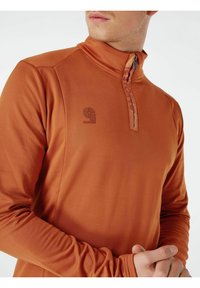 Dlouhý rukáv, pulovr se čtvrtinovým zipem v barvě spálené oranžové. Disponuje logem na hrudi a hladkou, elastickou texturou.