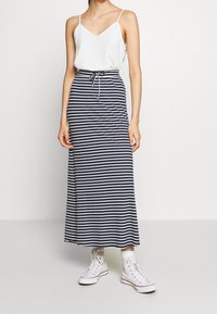 Randig, lång maxikjol i marinblått och vitt med elastisk midja och snörning. Kombinerad med en vit linne och vita sneakers.