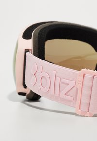 Suusagoodid, millel on helesinine rihm, millel on reljeefne "bliz" logo, must pehme sisemus ja rohelise tooniga objektiiv.