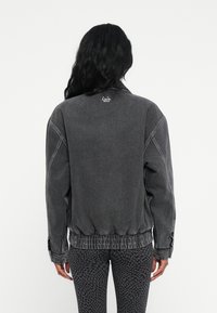 Siva denim jakna s sproščenim krojem, elastičnim robom in manšetami. Ima diskretno logo na vratu in teksturirano površino. Usklajena z vzorčastimi leginami.