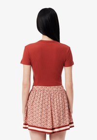 Haut rouge à côtes et à manches courtes associé à une jupe rose à motifs comportant des designs géométriques et un ourlet rayé.