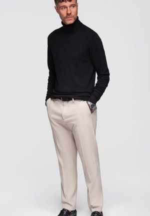 Pull à col roulé noir associé à un pantalon beige clair ajusté. L'ensemble présente une coupe classique et un tissu léger et lisse.