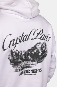 Felpa bianca con una grafica nera che raffigura montagne, alberi e una cabina, con il testo "Crystal Paris" e "NORDIC NIGHTS" in grassetto.