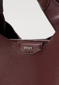 Burgundi tekstuuriga nahast käekott hõbedase tõmblukuga, millel on ees DKNY logo plaaster. Lihtne, kaasaegne disain ja tugevad rihmad.